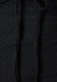 Tessuto nero con un motivo ondulato e strutturato. Il materiale appare leggero e leggermente spiegazzato, mostrando linee verticali distinte.