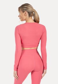 Langärmliges Cropped-Top und hoch taillierte Leggings aus leuchtend pinkem Stoff. Glatte Textur, figurbetontes Design und minimale Nähte.