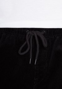 Pantaloni di velluto a coste neri con una vita regolabile tramite cordoncino, caratterizzati da righe verticali testurizzate e aglet neri sulle estremità dei cordoncini.