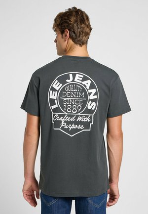 Grijs katoenen t-shirt met een grote witte afbeelding op de achterkant met de merknaam "LEE JEANS" en tekst die de kwaliteit en ambacht benadrukt.