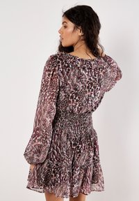Lila und weiße gemusterte Kleid mit schmalem Taillenbund, langen Puffärmeln und einem gestuften Rock. Leichter, fließender Stoff mit einer weichen Textur.