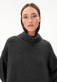 Pull en maille gris foncé avec un col haut et replié, à coupe ample. Il présente un matériau texturé et des coutures d'épaule tombantes.