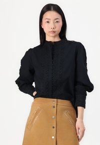 Musthave mustriga, millel on keeruline pitsdetail, kõrge krae ja nööpide esikülg. Kombineeritud beeži naha seelikuga, millel on nupud ja metallist aktsendid.