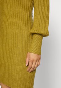 Robe en tricot côtelé à motifs de moutarde, dotée de longues manches avec des poignets ajustés, d'une coupe droite et d'une texture douce. Vue en gros plan de la manche et du côté.