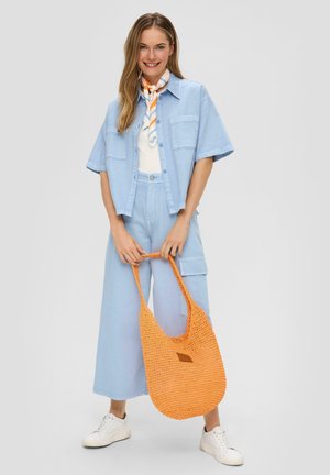 Chemise oversized bleu clair et pantalon large, associés à un sac en crochet orange texturé. Des baskets blanches complètent le look.