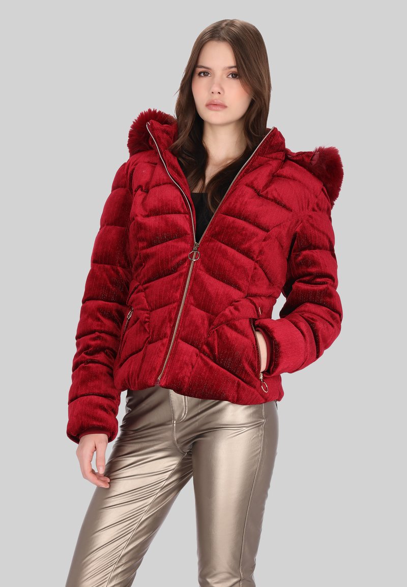 Červená nadýchaná bunda s texturovaným povrchem, předním zipem a kapucí. Má prošívaný vzor a kovové detaily. Nositelná se lesklými zlatými kalhotami.