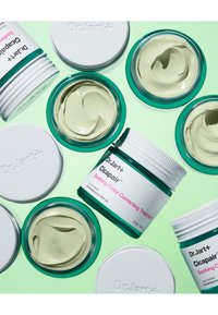 Dr. Jart+ Cicapair™ fargekorrigerende krem i klare glasskrukker med teal-detaljer; kremaktig lysegrønn tekstur synlig; hvite lokk med merkevare.