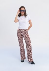 Witte t-shirt met korte mouwen en roze "No regrets" tekst, gecombineerd met bruine gestructureerde flared broeken. Zwarte sneakers maken de outfit compleet.