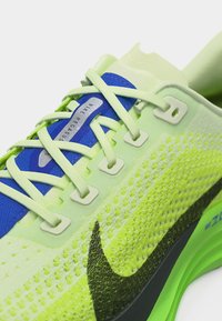 Približna slika tekaškega copata Nike Pegasus v neonsko zeleni barvi z črnim logotipom, svetlo zelenimi vezalkami in modrim jezikom z logotipom.