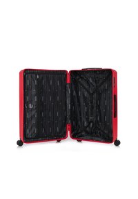 Valigia rigida rossa con interno a righe nere, dotata di tasche con zip e cinghie incrociate. Montata su quattro ruote per una facile mobilità.
