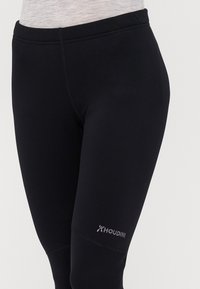 Leggings neri realizzati in materiale elasticizzato con un design aderente. Presentano un alto girovita e un logo Houdini discreto sulla parte inferiore della gamba.