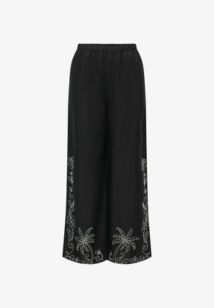 Czarne spodnie o szerokich nogawkach z elastycznym pasem, ozdobione białym kwiatowym haftem wzdłuż brzegu, wykonane z lekkiego, teksturowanego materiału.