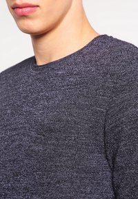 Suéter de punto en tono gris oscuro con cuello redondo, que presenta una mezcla de tejidos texturizados y sutiles variaciones de color para darle profundidad.