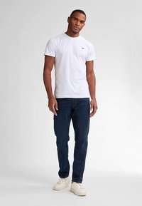 Bílé bavlněné tričko úzkého střihu s kulatým výstřihem; kombinováno s tmavě modrými džínami a bílými teniskami. Jednoduchý design bez viditelných vzorů nebo log.