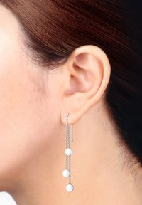 Boucles d'oreilles en argent pendantes avec trois disques ronds, suspendus à une chaîne, dotées d'un fermoir en crochet. Surface lisse et réfléchissante.