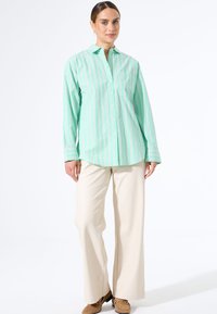 Groen gestreepte overhemdd met een kraag en lange mouwen, gecombineerd met beige wijde broek en bruine schoenen. Minimalistisch ontwerp details.