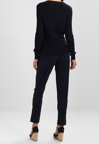 Marineblauwe kabelgebreide trui met lange mouwen, gecombineerd met donkere broek. Het model draagt sleehakken met een textuurrijke kurken zool.