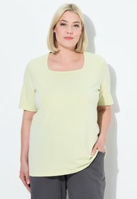 Top corto giallo chiaro a maniche corte con scollatura quadrata, realizzato in tessuto morbido. Abbinato a pantaloni grigi, dotati di tasche laterali. Design semplice.