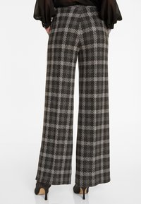 Wijdvallende broek in een grijs en zwart geruit patroon, gemaakt van een gestructureerde stof. Heeft een hoge taille en zijzakken.