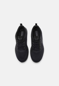 Chaussures de sport noires avec dessus en mesh, bout rond, lacets, languette au talon pour un enfilage facile et semelle en caoutchouc texturée.