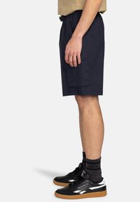 Shorts cargo blu navy, realizzati in tessuto a trama, con vita elastica, tasca laterale e taglio al ginocchio. Abbinati a sneakers nere.
