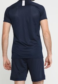 Man wearing navy blue athletic shirt and shorts, shown from the back against a plain white background.