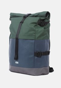 Rulltopp ryggsäck i mörkgrön och blå med en grå bas. Tillverkad av hållbart material, har justerbara remmar och spännen, minimalistisk logotyp.