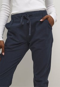 Pantalon bleu marine à cordon de serrage en tissu doux. Comprend des poches latérales et une coupe décontractée, avec des coutures visibles le long des coutures.