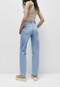 Vaqueros de pierna recta azul claro hechos de mezclilla, con bolsillos traseros de parche y cinturilla alta, combinados con sandalias de plataforma.