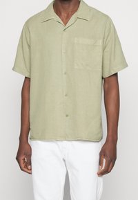 Chemise à manches courtes vert sauge avec boutons, en tissu doux. Comprend une poche plaquée et une coupe décontractée avec un col classique.
