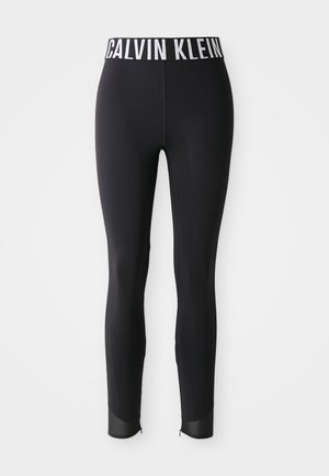 Black fitted leggings with white Calvin Klein logo waistband and mesh panel details at ankle hems against white background.