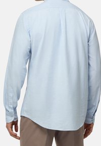 Ljusblå långärmad skjorta med rak fåll, knäppbara manschetter och standardkrage. Tillverkad av ett slätt, andningsbart tyg.