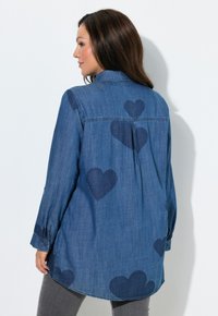 Denim blouse met een ontspannen pasvorm, voorzien van marineblauwe hartjespatronen. Lange mouwen met knoopdetail, een afgeronde zoom en een plooi aan de achterkant voor extra bewegingsvrijheid.