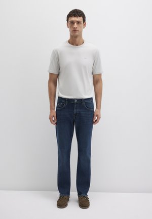 White short-sleeve t-shirt, blue jeans, and brown shoes. T-shirt features a small logo; jeans have traditional pockets and a straight leg design.