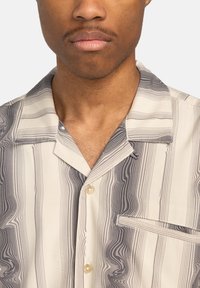 Short-sleeve shirt made of fabric with beige and gray swirling stripes, featuring a notch collar, chest pocket, and light buttons.