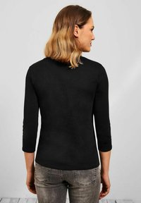 Schwarzes Langarmshirt mit rundem Halsausschnitt und figurbetonter Silhouette. Hergestellt aus weichem Stoff, wird es mit hellgrauen Jeans kombiniert.