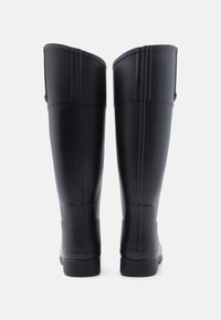 Ζευγάρι ψηλές μαύρες λαστιχένιες μπότες βροχής που στέκονται όρθιες σε λευκό φόντο, από την πίσω όψη.