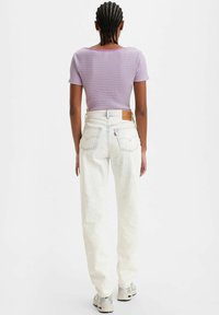 Top corto de cuadros morados ajustado, combinado con jeans blancos desgastados de cintura alta y zapatillas gris claro, visto desde la espalda.