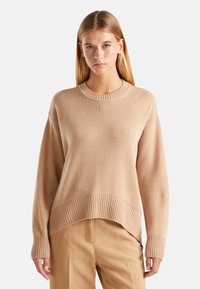 Beige oversized trui met een ribbellijn bij de hals en onderrand, met een gestructureerd breipatroon. Lange mouwen met ribbelmanchetten.