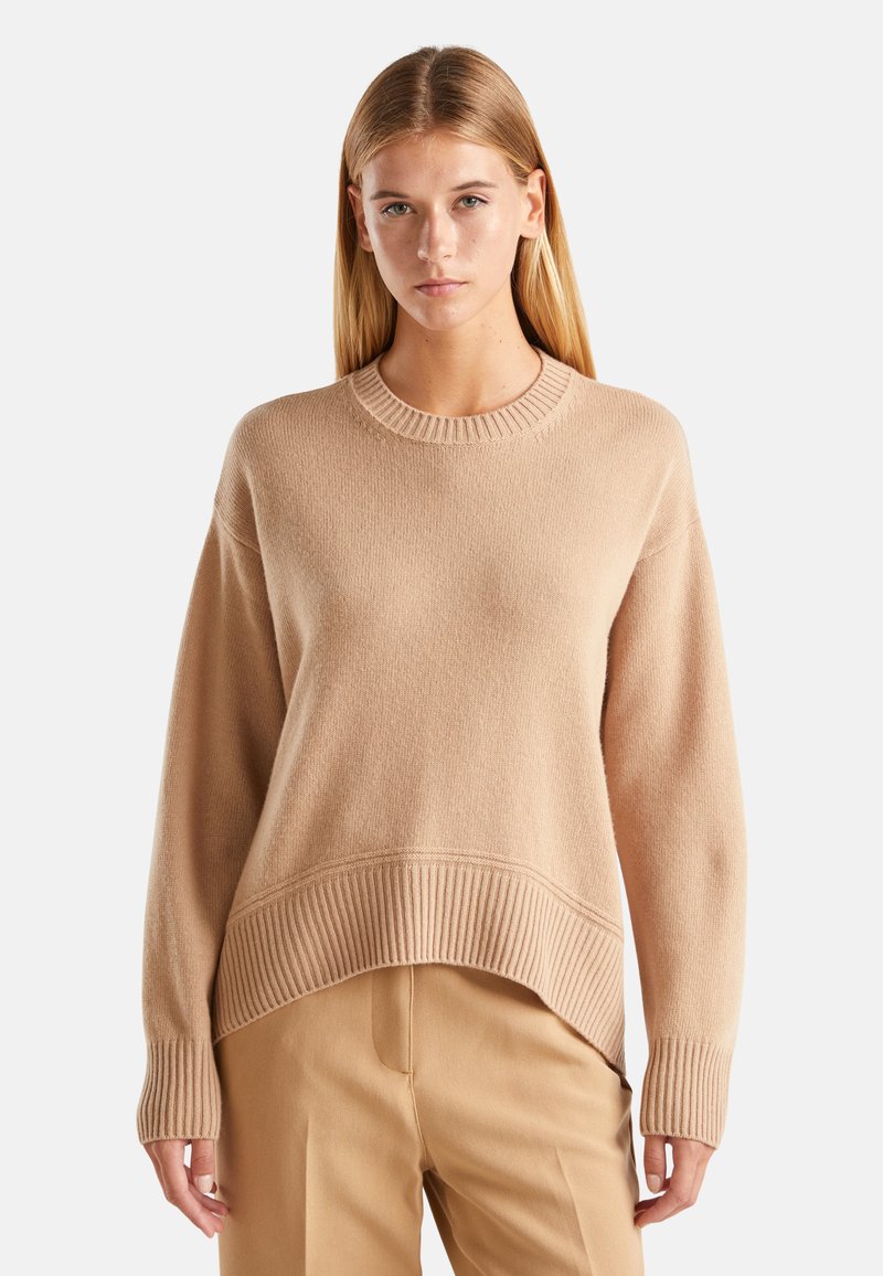 Beige oversized trui met een ribbellijn bij de hals en onderrand, met een gestructureerd breipatroon. Lange mouwen met ribbelmanchetten.