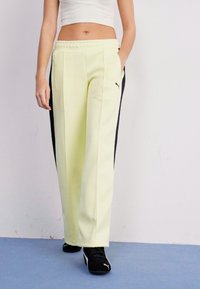 Light yellow track pants with black side stripes, elastic waistband, and PUMA logo accent on the left hip. Made from soft, smooth fabric.