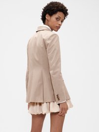 Blazer beige ajusté avec un col à revers, doté de manches longues et de poignets boutonnés, associé à une jupe légère rose pâle à volants.