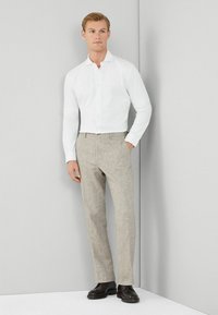 Witte overhemd met lange mouwen, gecombineerd met lichtbeige linnen broek en donkere schoenen. Eenvoudige, op maat gemaakte pasvorm en strakke lijnen.