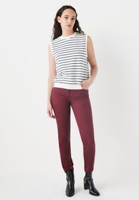 Top blanco sin mangas con rayas azul marino, combinado con pantalones burdeos y botas negras de tobillo. Tela suave con un corte ajustado.