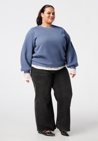 Blauwe sweatshirt met ballonsleeves en kantaccenten bij de mouwen, gecombineerd met hoge zwarte broek met wijde pijpen en zwart met studs versierde ballerina's.