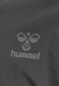 Tissu de vêtements de sport Hummel avec logo d'abeille en relief et nom de la marque, gros plan détaillé sur un matériau texturé et sombre.