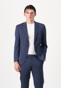 Morsko plavi odijelo od teksturirane tkanine s krojem po mjeri. Blazer ima dva gumba i rever, a dolazi uz odgovarajuće hlače.