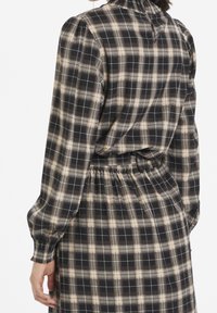 Checkered dress with black, beige, and white patterns. Fabric is soft, with a high neck and gathered waist. Long sleeves, elasticated cuffs.