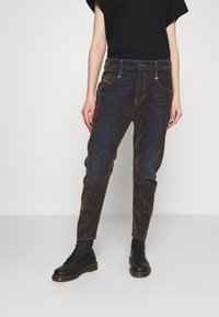 Donkerblauwe vervaagde denim jeans met een losse pasvorm, voorzien van beige stiksel en een vijf-pocket ontwerp. Draagt met zwarte veterschoenen.