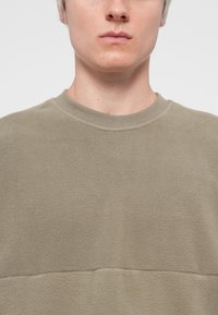 Lys olivengrønn sweatshirt laget av mykt, teksturert stoff. Har en rund hals og et enkelt, udevet design.